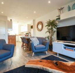 A living area with gray armchairs a wooden coffee table a flat screen tv and a dining table with chairs at Chy Fistral in Newquay
