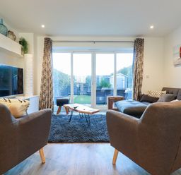 A living room with two armchairs a sofa a coffee table and a television with sliding glass doors leading to a garden at Chy Fistral in Newquay