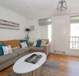 A living room with a sectional sofa blue and patterned cushions a marble oval coffee table and two windows at Skylark in Southwold