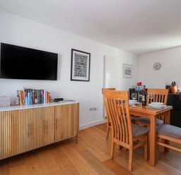 A dining area with wooden table and chairs a cabinet with books and a wall mounted TV at Skylark in Southwold