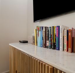 A white marble countertop with a row of books a tissue box a remote and a small wooden house decoration at Skylark in Southwold