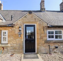 Stone cottage exterior with black door and white framed windows at Elm Cottage in Lucker near Warenford