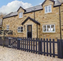 Stone house with black door and windows surrounded by black picket fencing and gravel at Oak Cottage in Lucker near Warenford