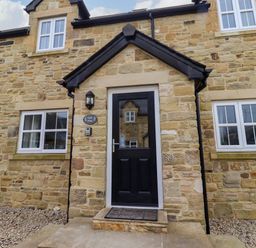 Front entrance with black door and stone walls at Oak Cottage in Lucker near Warenford