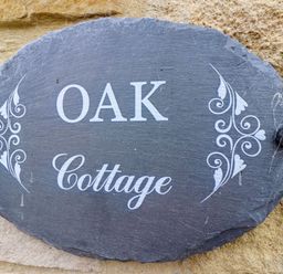 A stone sign with the text Oak Cottage mounted on a rough stone wall at Oak Cottage in Lucker near Warenford