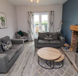 A living room with two grey sofas a round wooden coffee table a fireplace and glass doors leading outside at Oak Cottage in Lucker near Warenford