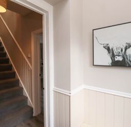 A hallway with carpeted stairs and a framed painting of a highland cow on the wall at Yew Cottage in Lucker near Warenford