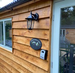 Exterior view of a wooden cabin with a window a black lantern a sign reading red squirrels drey and a keypad at Red Squirrels Drey Lucker near Belford