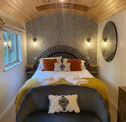 A bedroom with a bed with cushions and folded towels a sofa with a cushion a wall mirror and a television at Red Squirrels Drey in Lucker near Belford