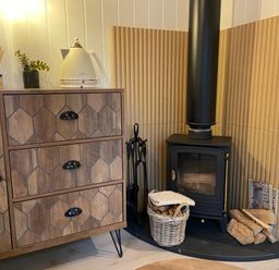 A wood stove with firewood and a wooden cabinet with a kettle and plant on top at Red Squirrels Drey in Lucker near Belford