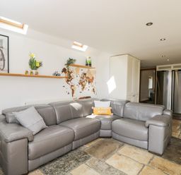 A living room with a gray leather sectional sofa under skylights and a wall shelf displaying decorations at 2 Dewars Farm Cottages in Middleton Stoney