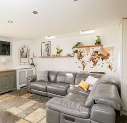 A living room with a gray leather sectional sofa TV on the wall and a world map on the wall at 2 Dewars Farm Cottages in Middleton Stoney