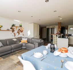 A kitchen and dining area with a gray sofa and a dining table set with dishes and pastries at 2 Dewars Farm Cottages in Middleton Stoney