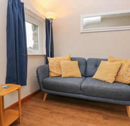 A sitting area with a blue sofa with yellow cushions a floor lamp a window with blue curtains and a small orange side table