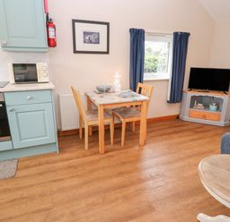 A kitchen and dining area with a table and two chairs a microwave oven a television on a stand and a window with curtains at Ramblers Rest in St Just