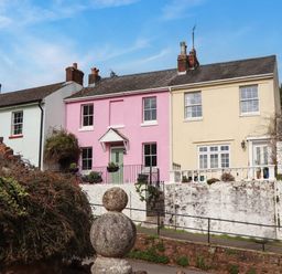 A street view of three attached houses with pastel colored walls and a stone wall in front at Rose Cottage in Bishopsteignton