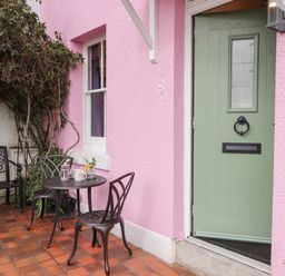 An outdoor patio with a small metal table and chairs next to a pink wall and green door at Rose Cottage in Bishopsteignton