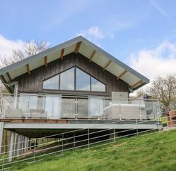 A chalet-style house with a glass-railed balcony on a grassy hillside at Barcud Coch - Red Kite in Garthmyl