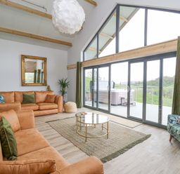 A living room with large windows a glass coffee table and brown sofas at Barcud Coch - Red Kite in Garthmyl