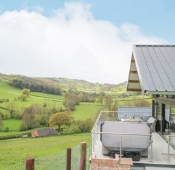 A balcony with outdoor seating and hot tub overlooking green hills and fields at Barcud Coch - Red Kite in Garthmyl
