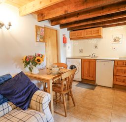 A kitchen and dining area with wooden cabinets a tiled floor a small table with chairs and flowers on the table at Ty Bach Twt Synod Inn near New Quay