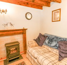 A sitting room with a plaid sofa a wood-burning stove and a clock on the wall at Ty Bach Twt Synod Inn near New Quay