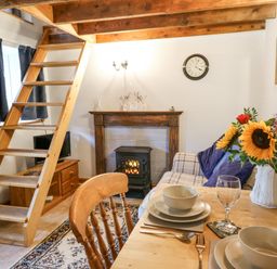 A living room with wooden stairs next to a fireplace a dining table set with dishes and a vase of flowers at Ty Bach Twt Synod Inn near New Quay
