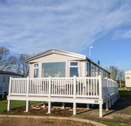 A mobile home with a white railing deck on a grassy plot with other mobile homes nearby at 17 Summer Meadows in Ashington