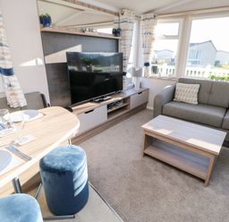 A living room with a gray sofa a wooden coffee table a TV on a stand and a dining table with two blue stools at 17 Summer Meadows in Ashington
