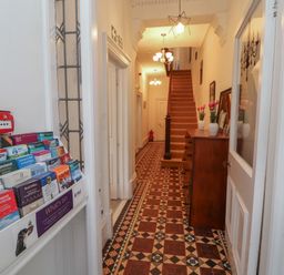 A hallway with a patterned tiled floor a chest of drawers with vases and flowers stairs and a brochure stand at The Furness Haven in Barrow-In-Furness