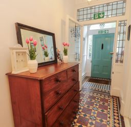 A hallway with a wooden chest of drawers a mirror vases with flowers and a blue door at The Furness Haven in Barrow-In-Furness