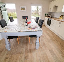 A kitchen with a dining table covered with a plastic tablecloth and six chairs next to cabinets and a stove at The Poets Cottage in Portglenone