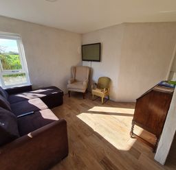 A living room with a sectional sofa two chairs a wall-mounted television and a wooden cabinet at The Poets Cottage in Portglenone
