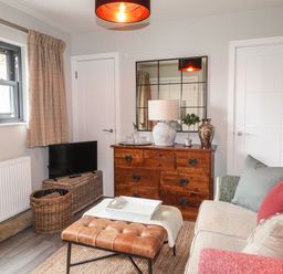 A living room with a sofa cushions leather ottoman wooden dresser and a small TV at The Pottery in Newport Pembrokeshire