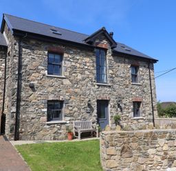The front view of a stone house with grey windows a bench and a low stone wall at The Pottery in Newport Pembrokeshire