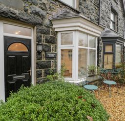 A stone exterior of a house with a black door a bay window and two metal chairs at Bronwen House in Llanbedr