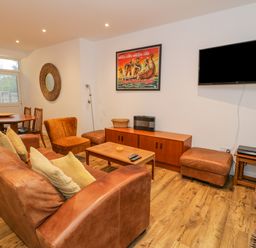 A living room with leather sofa and chairs a wooden dining table and TV on the wall at Bronwen House in Llanbedr