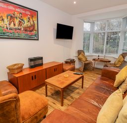 A living room with brown leather sofa and armchair wooden coffee table and two wicker chairs near a bay window at Bronwen House in Llanbedr