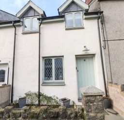 A white house with two dormer windows a green door numbered 4 and a small garden in front at Ty Crydd in Llansaint near Kidwelly