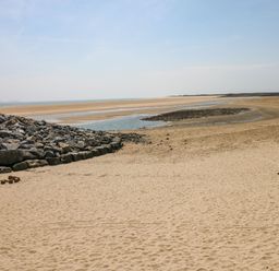 A sandy beach with a pile of rocks on the left and the ocean in the background at Ty Crydd in Llansaint near Kidwelly