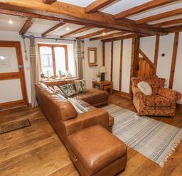A living room with a brown leather sectional sofa red patterned armchair wooden beams and floor at Ty Crydd Llansaint near Kidwelly