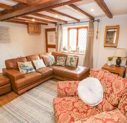 A living room with brown leather sectional sofa and red patterned armchair at Ty Crydd in Llansaint near Kidwelly