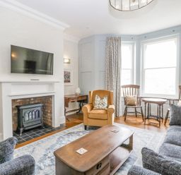 A living room with a fireplace a wall mounted TV a brown armchair wooden chairs and a coffee table at Belle Vue in Hay on Wye Herefordshire