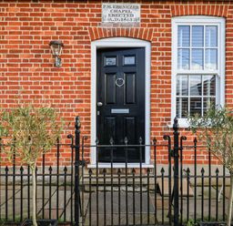 A black door and two windows on a red brick building with a black metal fence and two small trees at Ebenezer Chapel in Knodishall nr Saxmundham