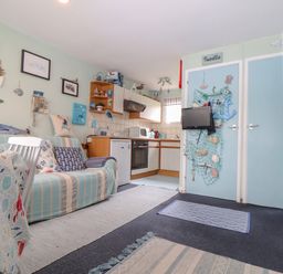 A small living area and kitchen with a striped sofa and mounted TV at Villa 29 in Camelford