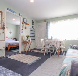 A small living and dining area with a table and chairs next to a window and a striped sofa with cushions in Villa 29 Camelford