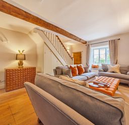 A living room with sofas orange cushions and a window at Lynton Cottage in Enstone