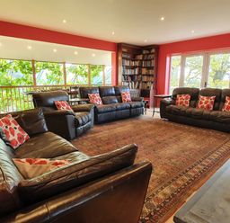 A living room with leather sofas and bookshelves near large windows at Cringoed House Llanarth near Aberaeron