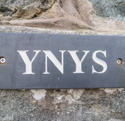 A black rectangular sign with the text YNYS mounted on a stone wall at Ynys in Dyffryn Ardudwy