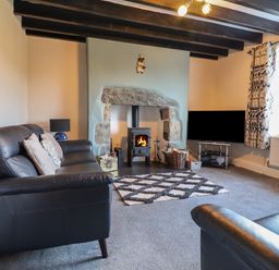 A living room with a black leather sofa a wood burning stove and a television at Ynys in Dyffryn Ardudwy